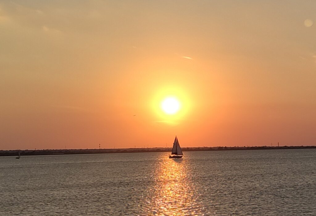 sailboat at Lake Hefner with sun directly behind the boat, hazy yellowish sky